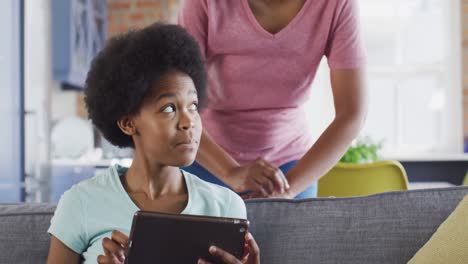madre y hija afrodescendientes felices sentadas en el sofá usando una tableta