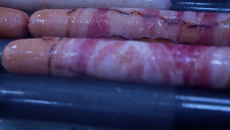 prosciutto envuelto en perros calientes cocina en rodillos calientes en el mostrador de delicatessen
