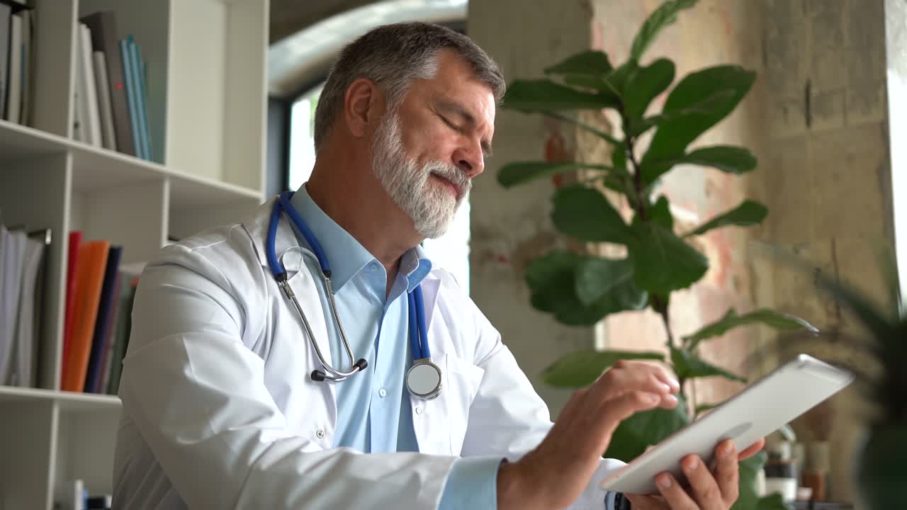 Medico senior che riflette sulla diagnosi del paziente e digita su un tablet. Il suo ufficio è luminoso e moderno.