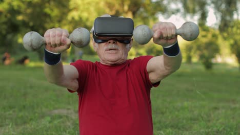 Senior-old-grandfather-man-in-VR-headset-helmet-making-fitness-exercises-with-dumbbells-in-park