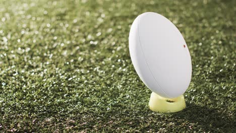 white rugby ball on kicking tee on sunlit grass with copy space, slow motion