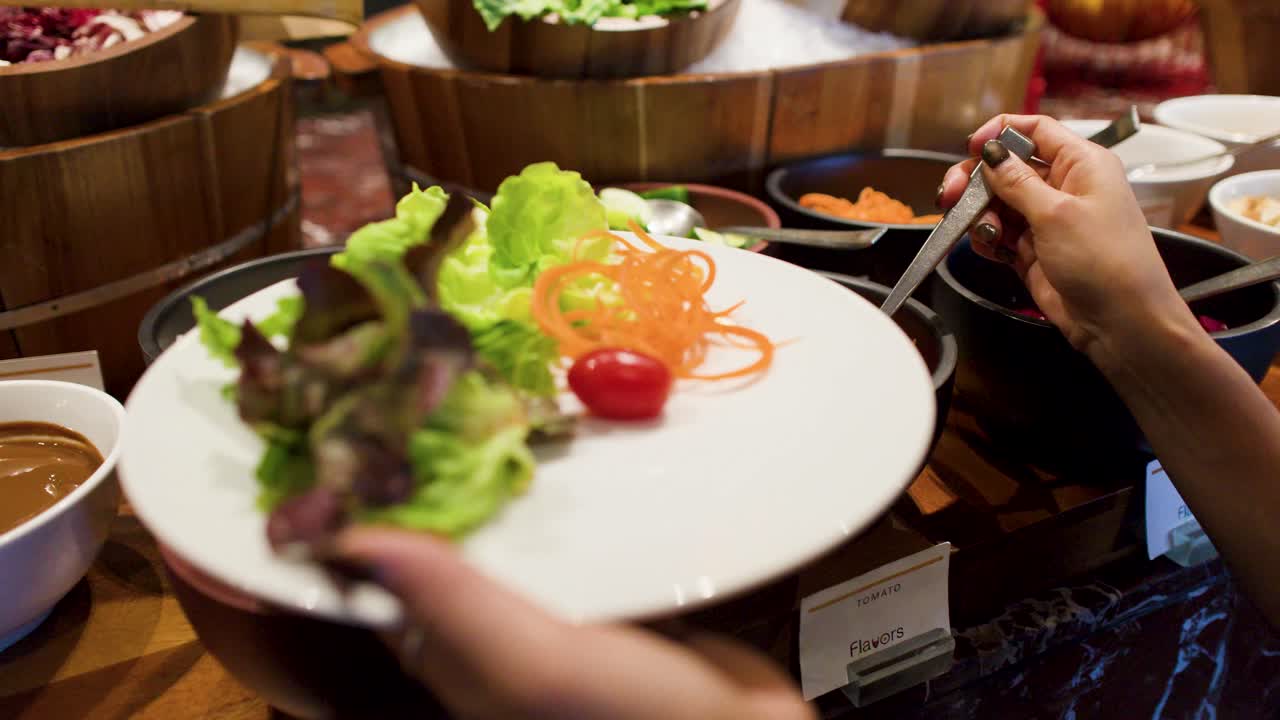 Primo piano di mani che usano un cucchiaio per posizionare pomodorini su un piatto da insalata.