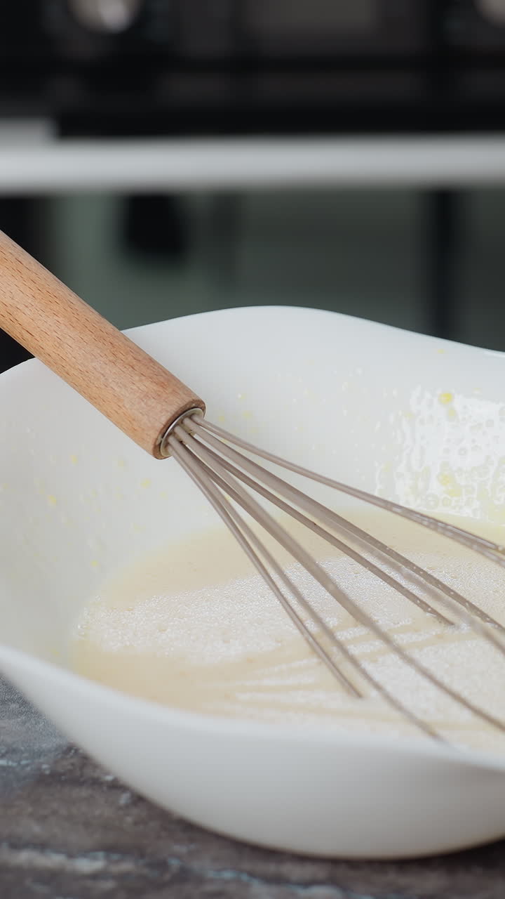 batido descansando en la mezcla de horneado dentro de un cuenco blanco en la encimera, el fondo de la cocina cuenta con gabinetes modernos, horno y espacio de trabajo limpio, creando una atmósfera de horno casera