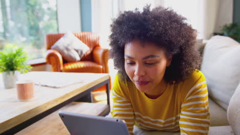 mujer relajándose en el sofá en casa usando una tableta digital para transmitir películas