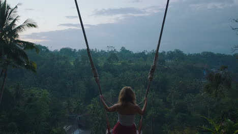 happy woman swinging over tropical jungle at sunrise travel girl enjoying exotic vacation sitting on swing in having fun holiday lifestyle freedom 4k