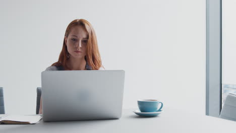 joven mujer de negocios vestida casualmente trabajando en una computadora portátil en una oficina moderna tomando llamadas por teléfono móvil