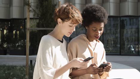 Relaxed-women-with-smartphones-talking-on-street