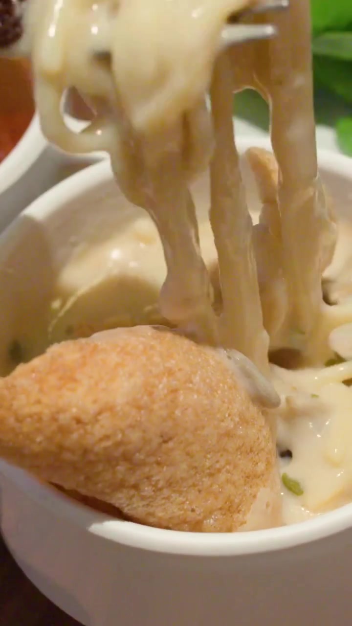 Primo piano verticale di una forchetta che solleva noodles al formaggio da una ciotola con antipasti fritti.