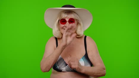 Senior-woman-tourist-in-swimsuit-bra-wearing-red-sunglasses,-waving-hands-hi-hello-welcome-greetings