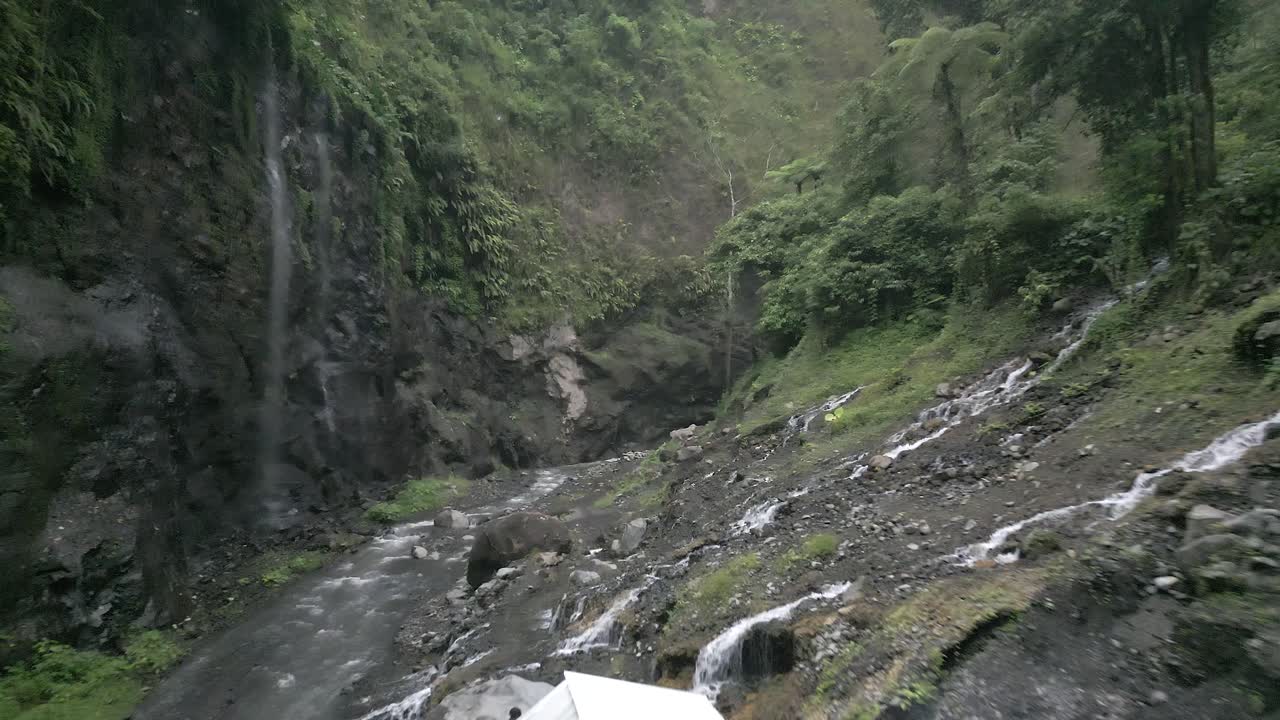 Low aerial flies up hazy steep narrow jungle canyon on Java, Indonesia