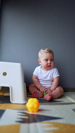 lovely baby boy sitting at the wall looks at the toy in front of him. infant kid playing with balls at home. vertical video.