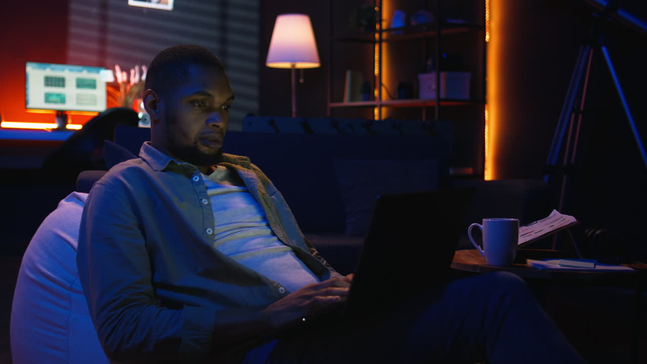 Vertical Video Adult man typing on laptop while he lays on a bean bag at home