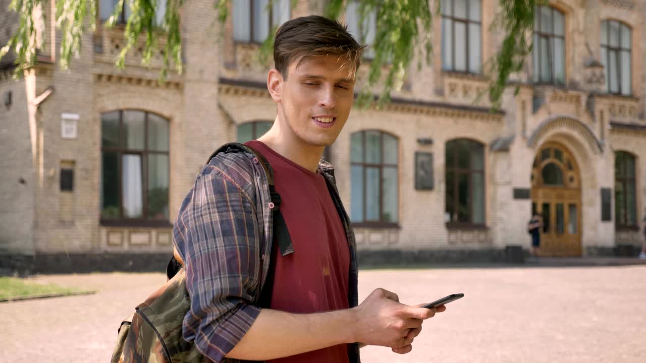 젊은 잘생긴 남자가 여름에 낮에 공원에서 스마트폰으로 타이핑하고, 카메라를 보고, 의사소통 개념