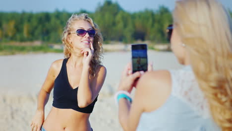 woman photographing his girlfriend on the beach using cell phone