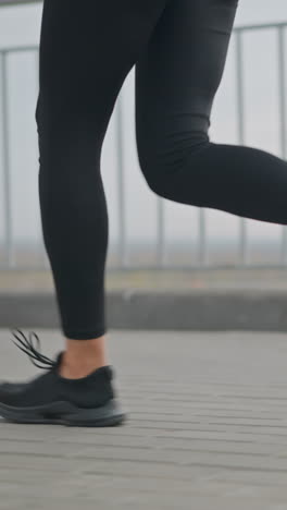 close-up view of woman s legs jogging for morning fitness in black leggings and black sneakers, showing active workout routine on paved path with iron fence in background