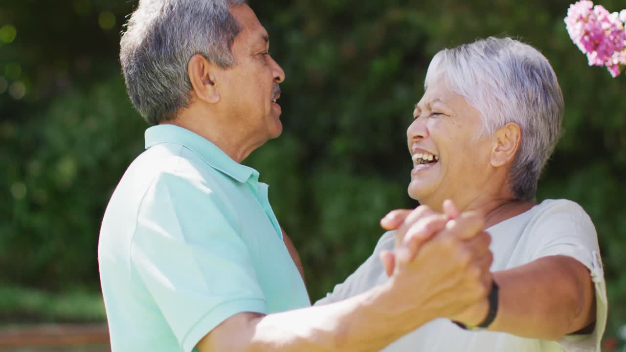 정원에서 손을 잡고 춤을 추는 행복한 두 인종의 노인 커플의 비디오