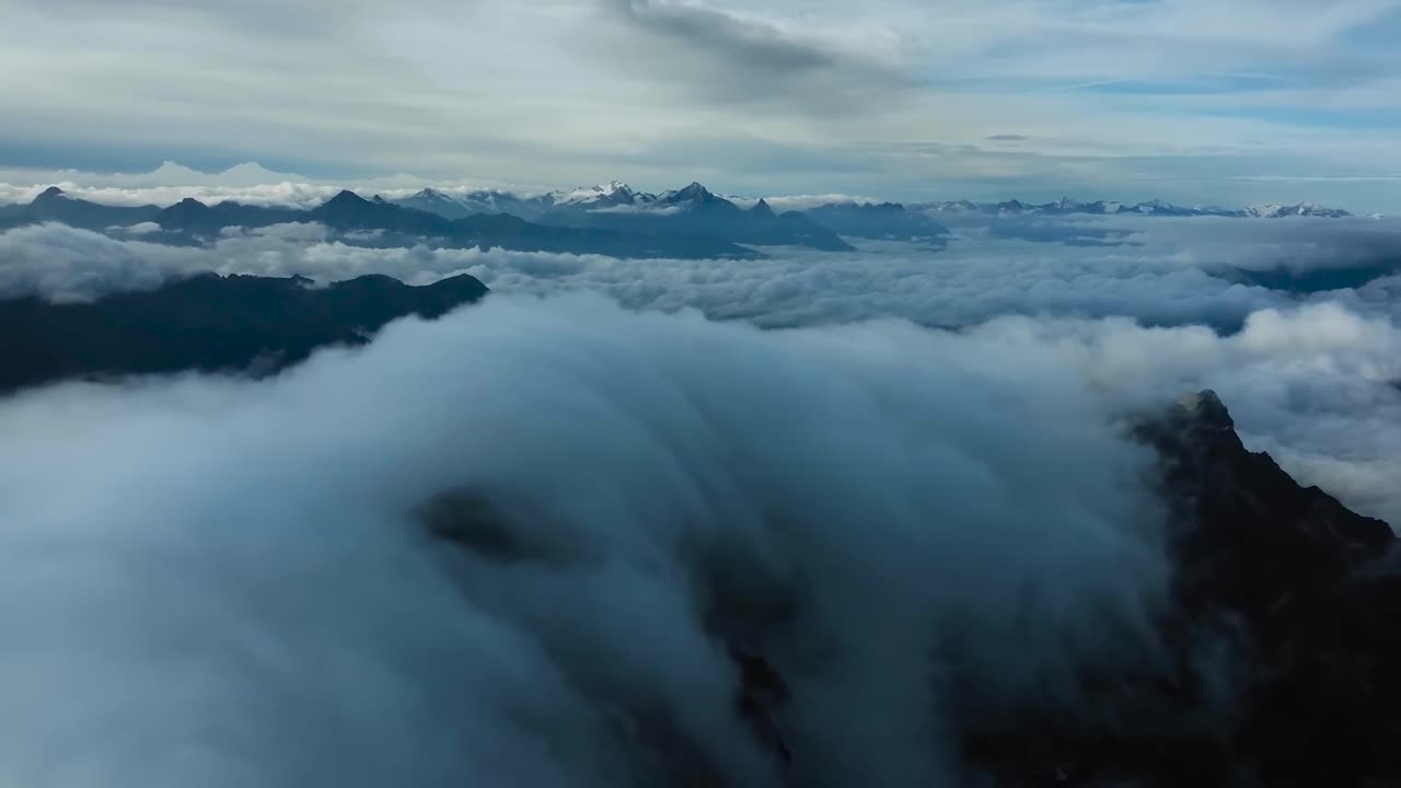 Aerial drone flying above white fluffy clouds at Western Alps Italy during a beautiful day. The footage pans right to left revealing tall mountain tops and blue sky in the background with more clouds.