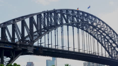 Turistas-Escalando-El-Puente-Del-Puerto-De-Sydney-Mientras-Las-Banderas-Aborígenes-Y-Australianas-Ondean-Sobre-Sus-Cabezas,-En-Australia