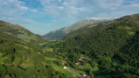 drone flight in a small valley visualizing a village with its path and crop and livestock meadows with its oak and beech forests with a background of limestone mountains in cantabria-spain