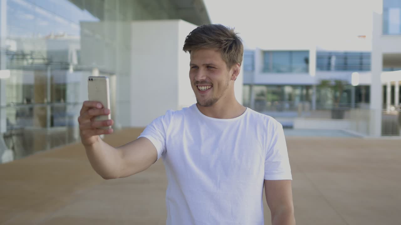 Handsome young guy wearing white t-shirt taking selfie outdoor.