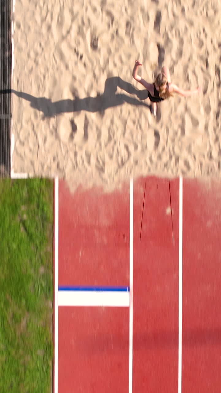 Ripresa verticale con drone di una giovane donna che pratica il salto in lungo su una pista di atletica professionale. Ideale per contenuti su sport, fitness e allenamento.