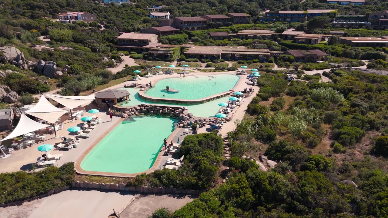 Vista aérea de piscinas de resort rodeadas por vegetação exuberante e vilas num dia ensolarado
