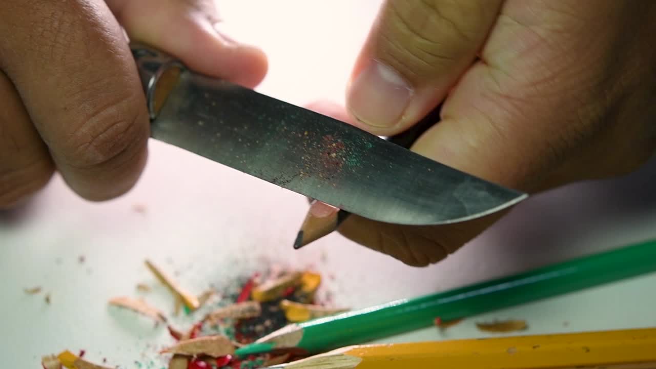 Opptak av hender som sakte spisser en blyant og noen fargeblyanter med en skarp kniv