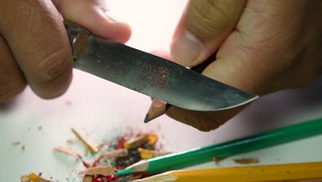 imágenes de manos afilando lentamente un lápiz y algunos lápices de colores con un cuchillo afilado