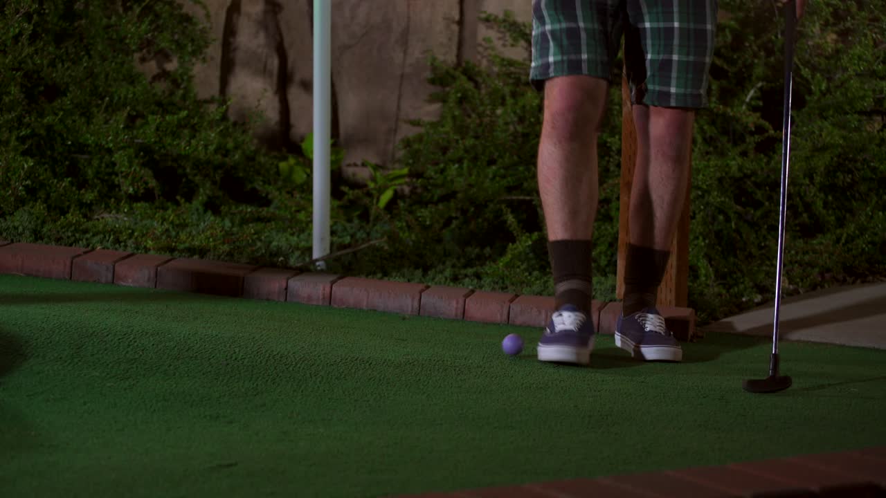 보라색 미니 골프공이 클럽에 부딪히는 것을 클로즈업하고 샷이 끔찍하고 공이 골퍼에게 다시 굴러옵니다