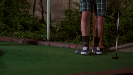 un primer plano de una mini pelota de golf morada que es golpeada con un palo y el tiro es horrible y la pelota vuelve rodando hacia el golfista