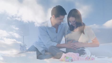 animation of clouds over happy caucasian man embracing pregnant wife