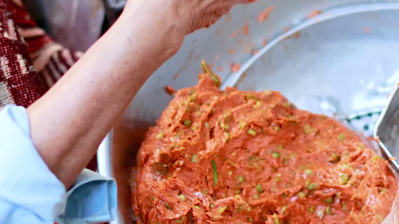 Close-up of hands shaping a spiced fish mixture in a large metal bowl.