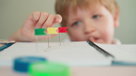 Toddler-boy-reaches-to-red-flag-on-pin-by-fingers-at-table