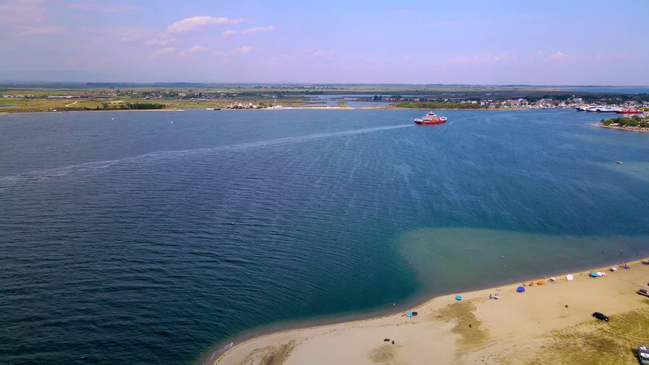 clip aéreo moviéndose hacia abajo sobre una playa tropical con arena dorada y un ferry avanzando en el área de keramoti, kavala, en el norte de grecia en 4k