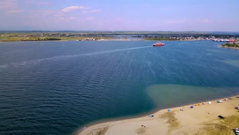 Clip-Aéreo-Moviéndose-Hacia-Abajo-Sobre-Una-Playa-Tropical-Con-Arena-Dorada-Y-Un-Ferry-Avanzando-En-El-área-De-Keramoti,-Kavala,-En-El-Norte-De-Grecia-En-4k