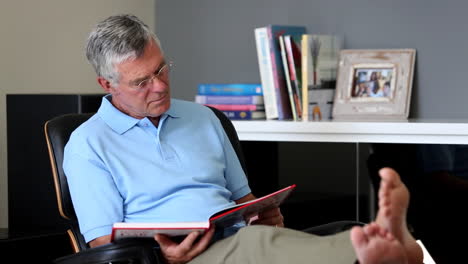 barefoot man relaxing on a chair while reading a book