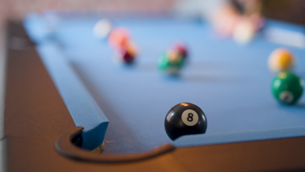 Eight ball and cue ball on blue pool table under soft indoor lighting, shallow focus