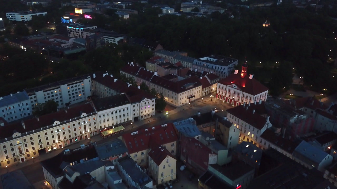Foggy night aerial shot of the Tartu Town Hall Square with glowing evening lights and mist.
