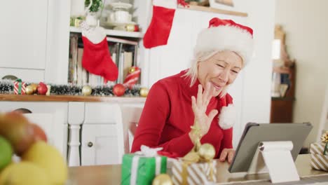 Happy-senior-caucasian-woman-wearing-santa-claus-hat,-using-tablet-for-video-call