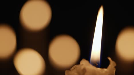 wax burning candle flickers in dark on a black background with blurred candlelight bokeh effect. background or illustration of remembrance, mourning or celebration. blaze candles in church close up