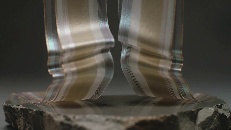 Top actuators lowering metallic ribbons, lower thirds flexing and curling above rough stone slab
