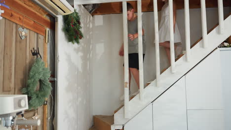 kids in casual wear coming down white staircase with holiday decorations in background, festive atmosphere in home, children excited for holiday season, joyful family moment during christmas