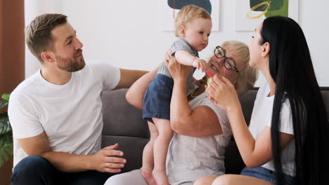 happy parents and grandmother playing with child sitting on sofa in living room