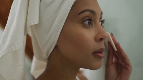 Mixed-race-woman-wearing-towel-on-head-cleaning-her-face
