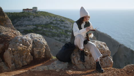 romantic girl reading book on rocky mountain vertical. tourist rest ocean cliff