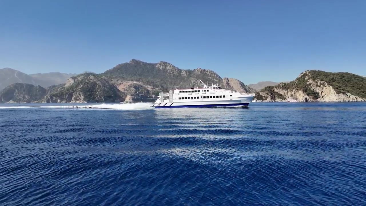 Turchia, Marmaris. Traghetto di Rodi che entra nella Baia di Marmaris in una giornata di sole con cieli azzurri e senza nuvole. Schizzi bianchi dietro il traghetto su un mare calmo e di un blu profondo.