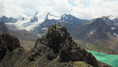 Man-standing-on-a-mountain-range-overlooking-the-Ala-Kol-lake,-Kyrgystan,-Beautiful-view,-great-achievement,-orbiting-drone