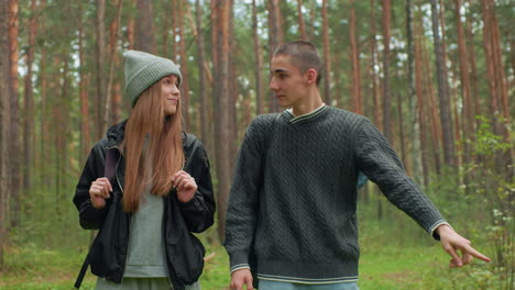 botanists strolling through forest, casually engaged as one shows something to friend while walking side by side among trees, both carrying travel bags in green woodland