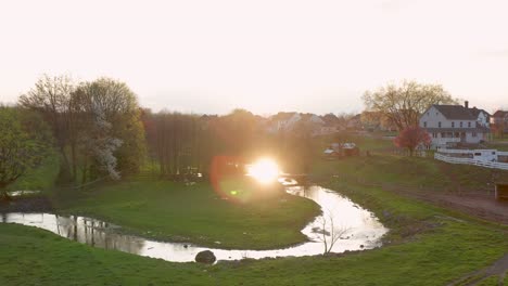 Aerial-captures-reflection-of-sun-in-stream-water-flowing-through-rural-farmland-in-USA