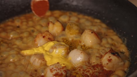 enhancing the flavor of the seafood dish by adding red paparika spice powder and creme fraiche into bubbling pan, cooking delicious scallop gratin, close up shot